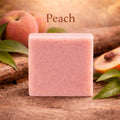 Pink soap bar with peach slices and leaves on a wooden background