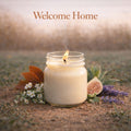Candle in a jar with flowers and leaves on sand, 'Welcome Home' text above